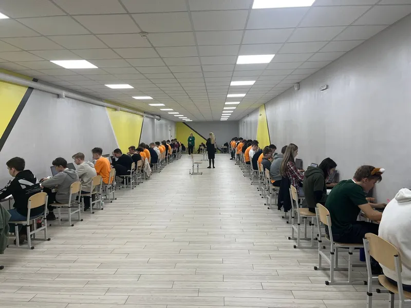 Contestants at laptops in two rows along a long hall during a round